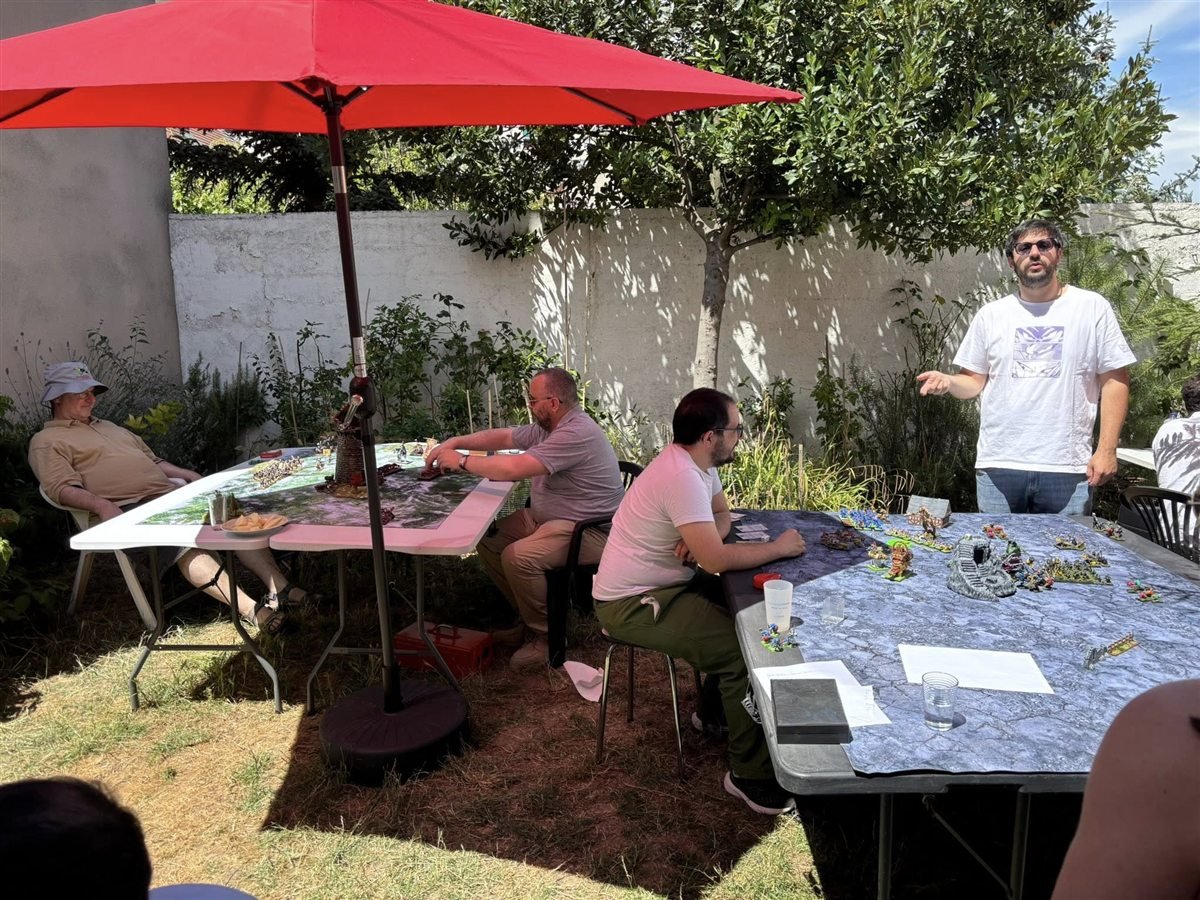 Joueurs installes autour d'une table de figurines sous un parasol